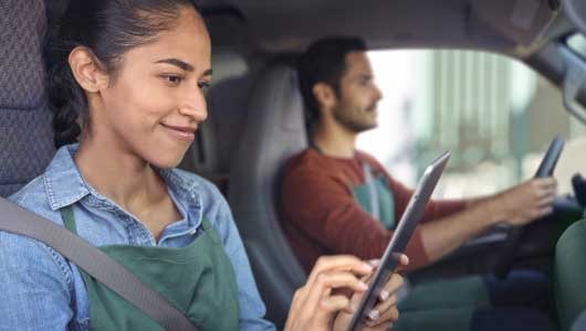 Two People Sitting in a Car with the Passenger Looking at a Tablet