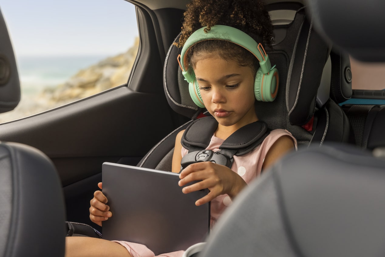 Child in the Backseat With Headphones on and on a Tablet 