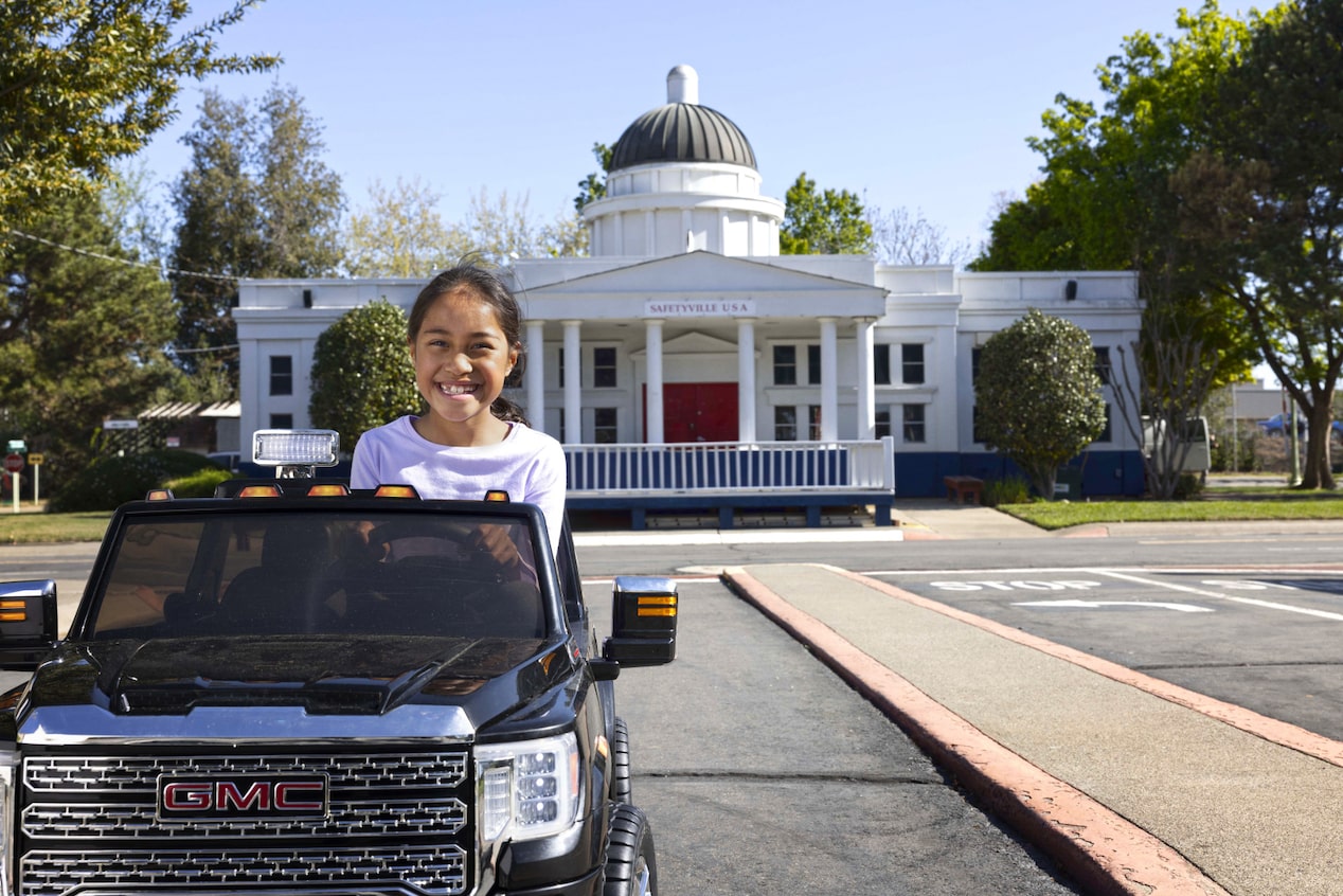 Young Girl Riding Away From a House in a Play GMC Car