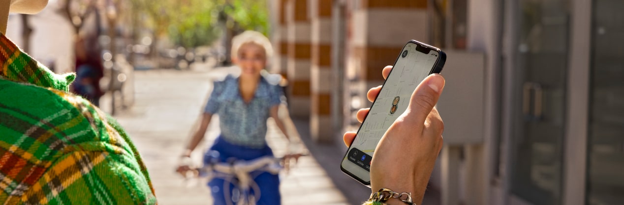 Woman in Distance Riding Bike Towards Man Holding Smartphone 