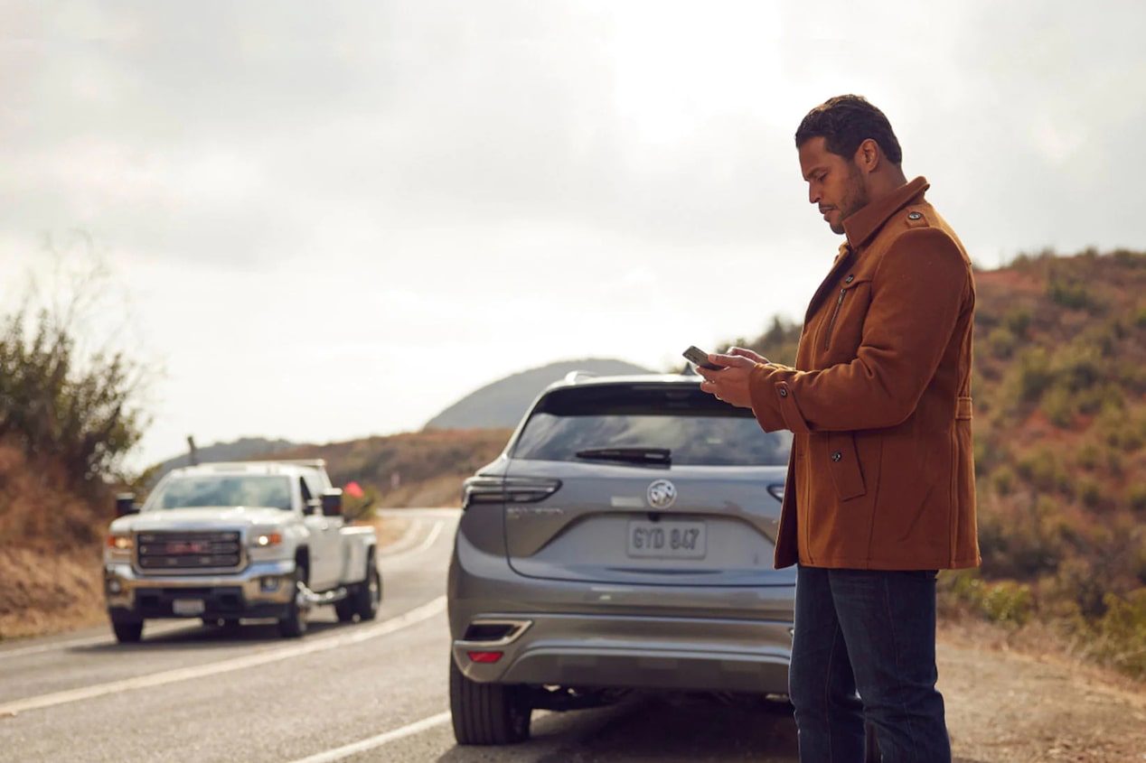 A man standing next to his car on the side of the road waiting for roadside assist