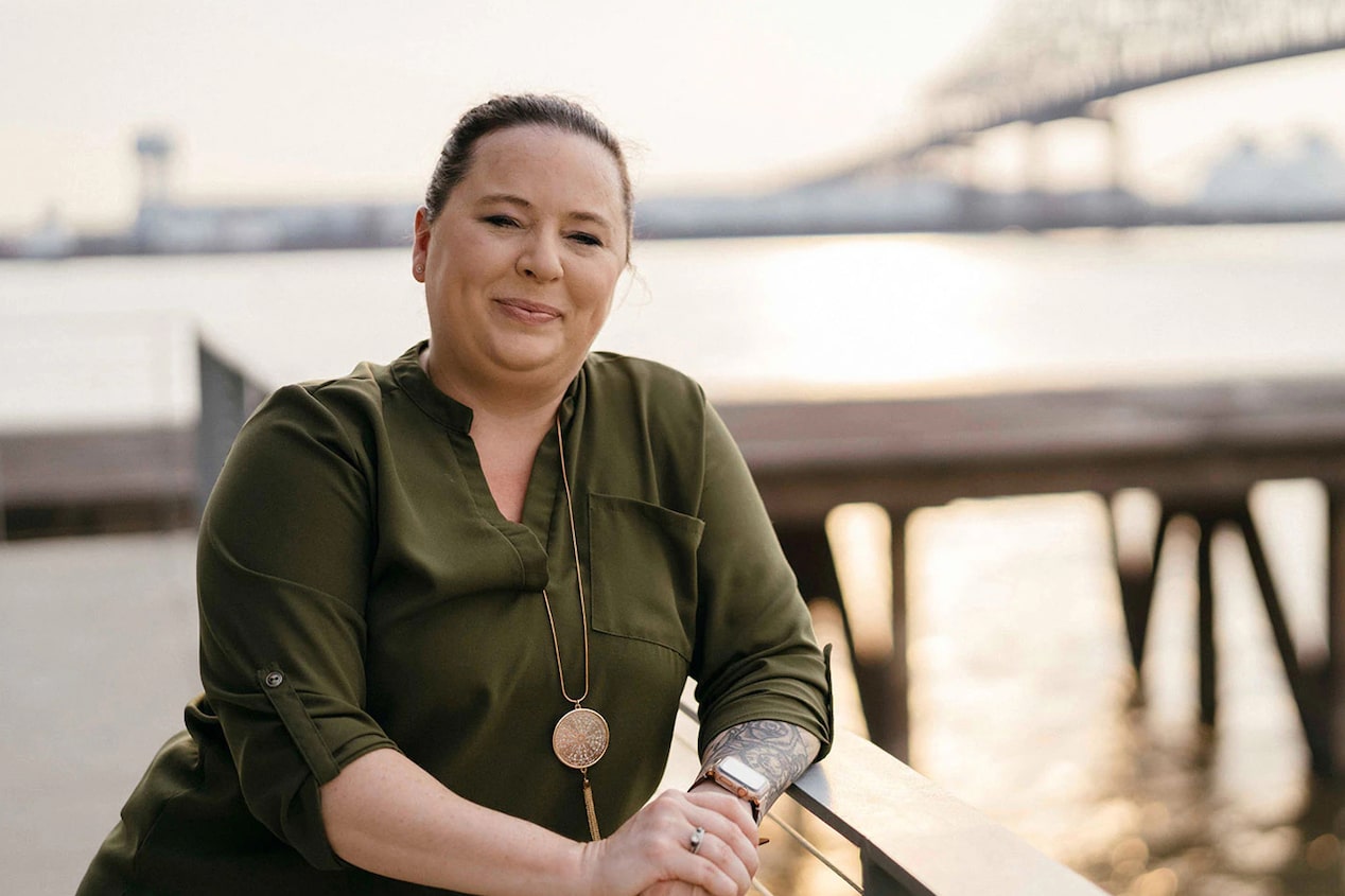 woman leaning on dock in front of small bridge smiling on camera