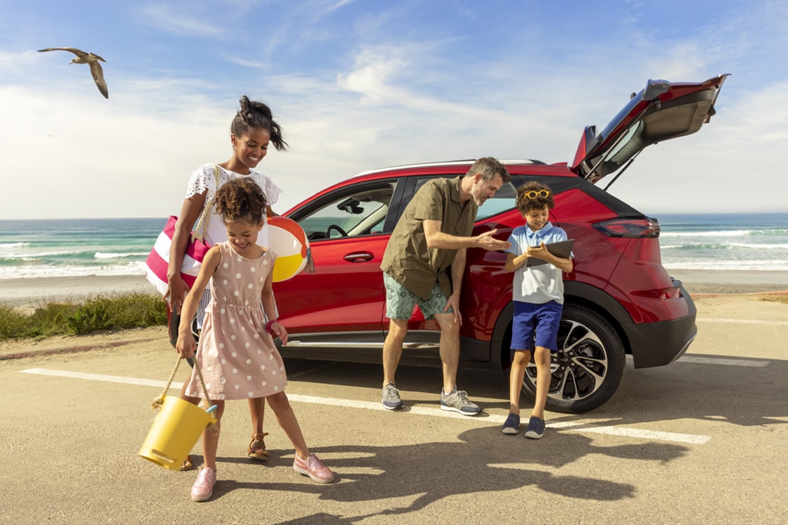 Family at the Beach Near GM SUV Checking Online Devices