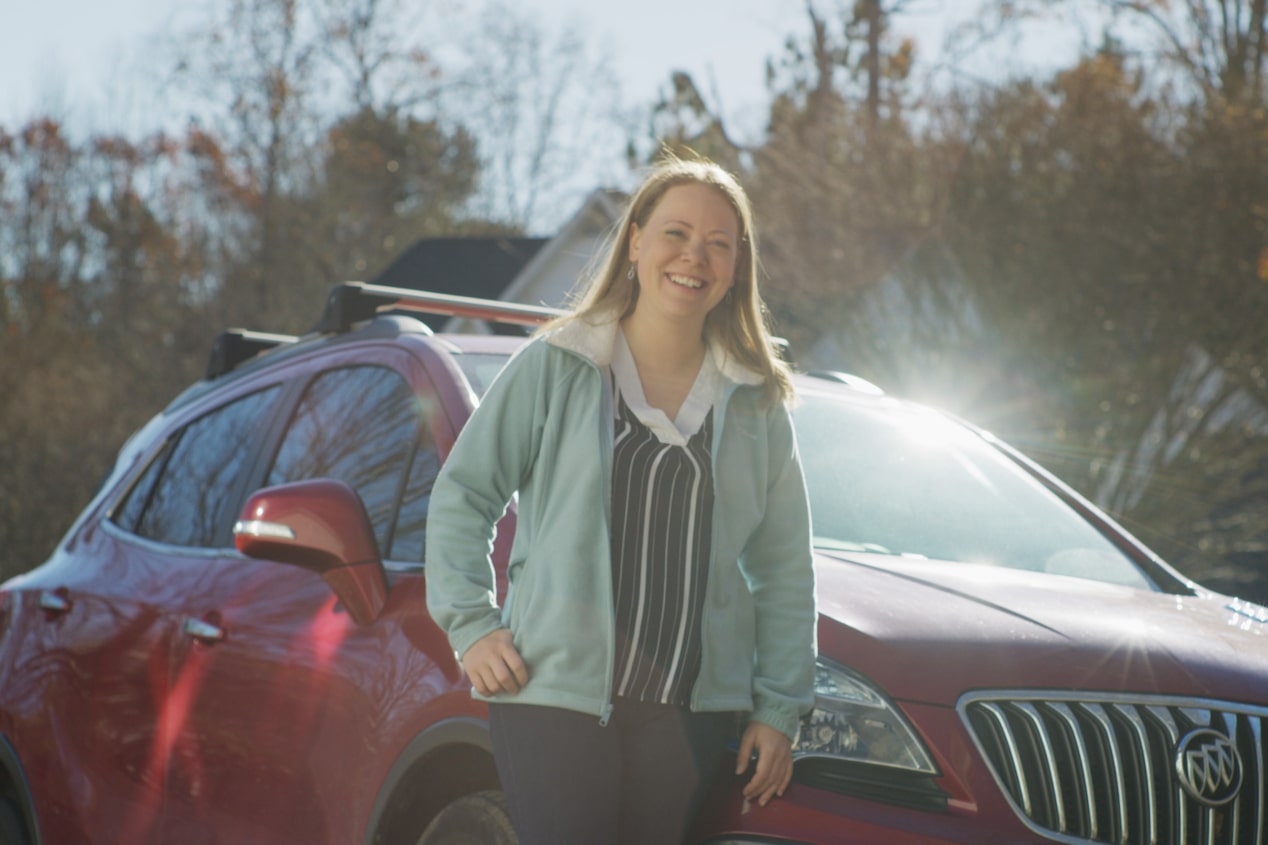 Woman Smiling and Leaning on the Hood of her Vehicle