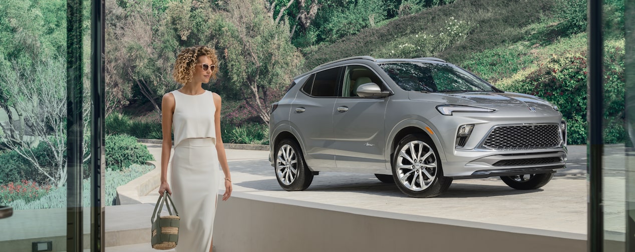 A woman walking into her house with her Buick vehicle parked in the driveway