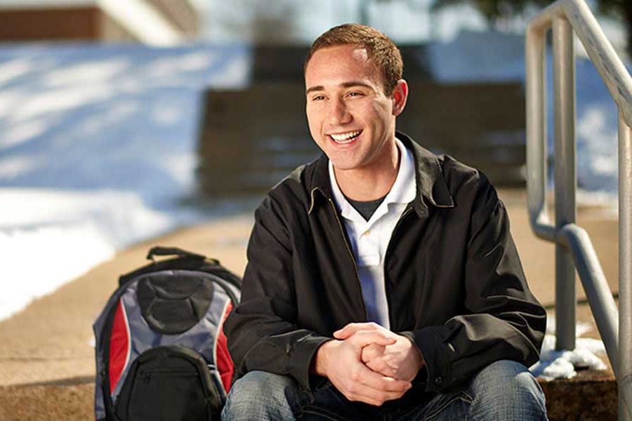 Man Smiling & Sitting on Steps With Backpack