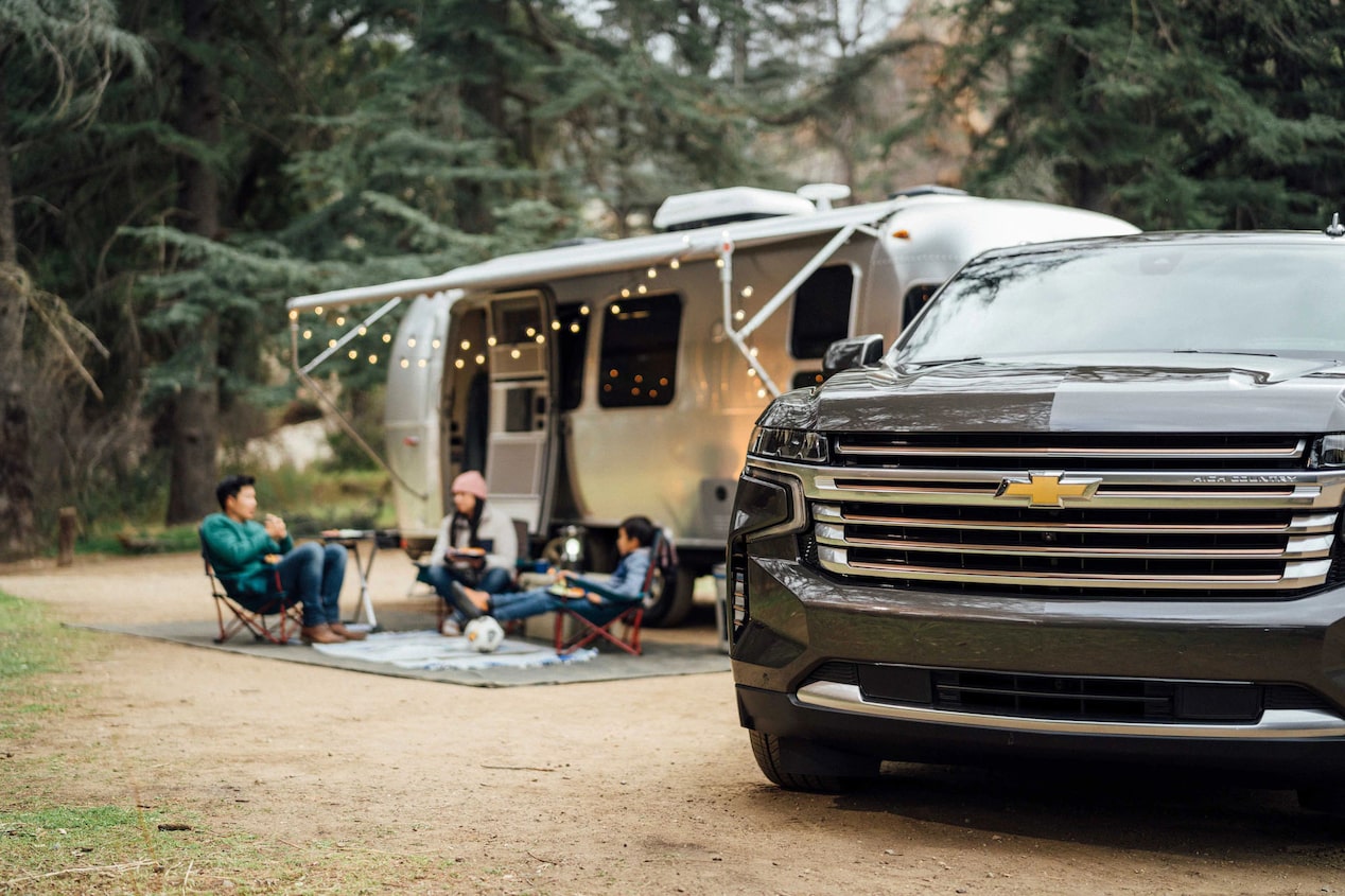 Family of Three Sitting Together Outside the Camper Next to Chevy Vehicle