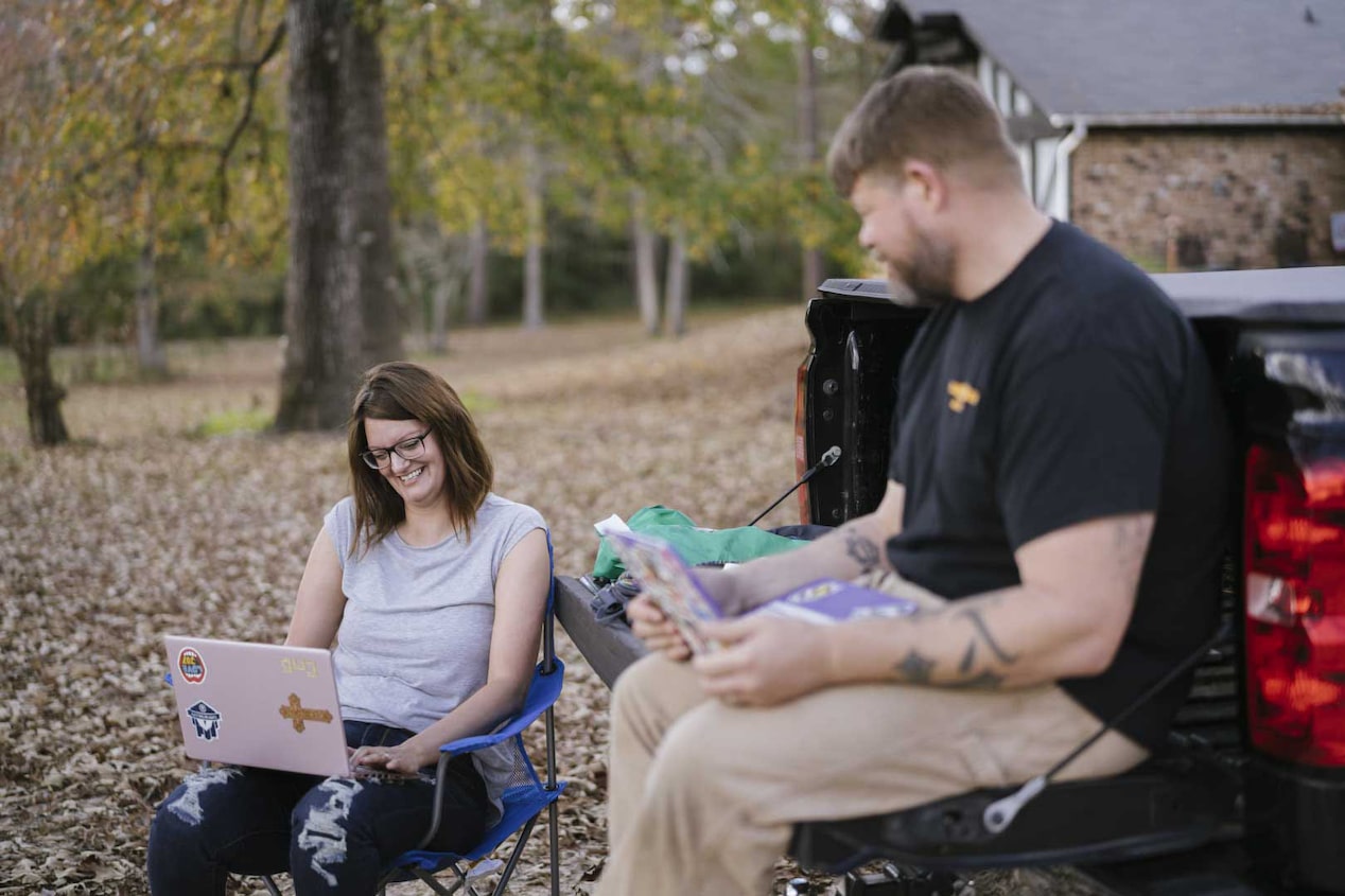 Man and Women Sitting at Tailgate of Chevy Pickup Truck on Laptops