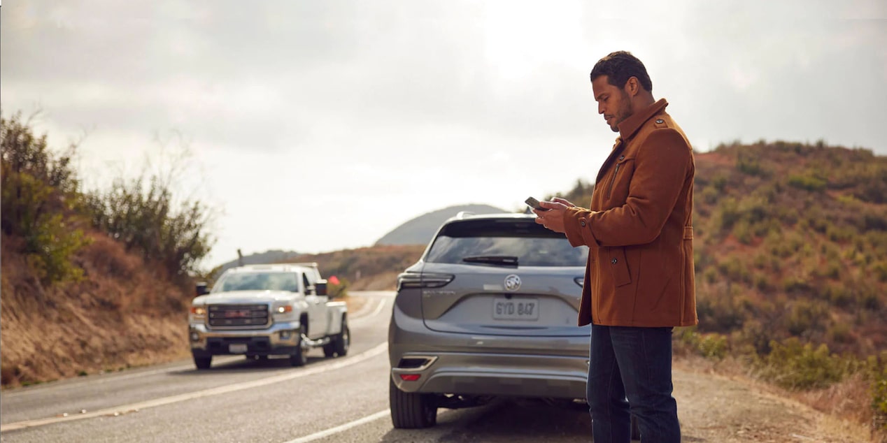 Man Standing Next to Vehicle on the Side of Road Using Smartphone  