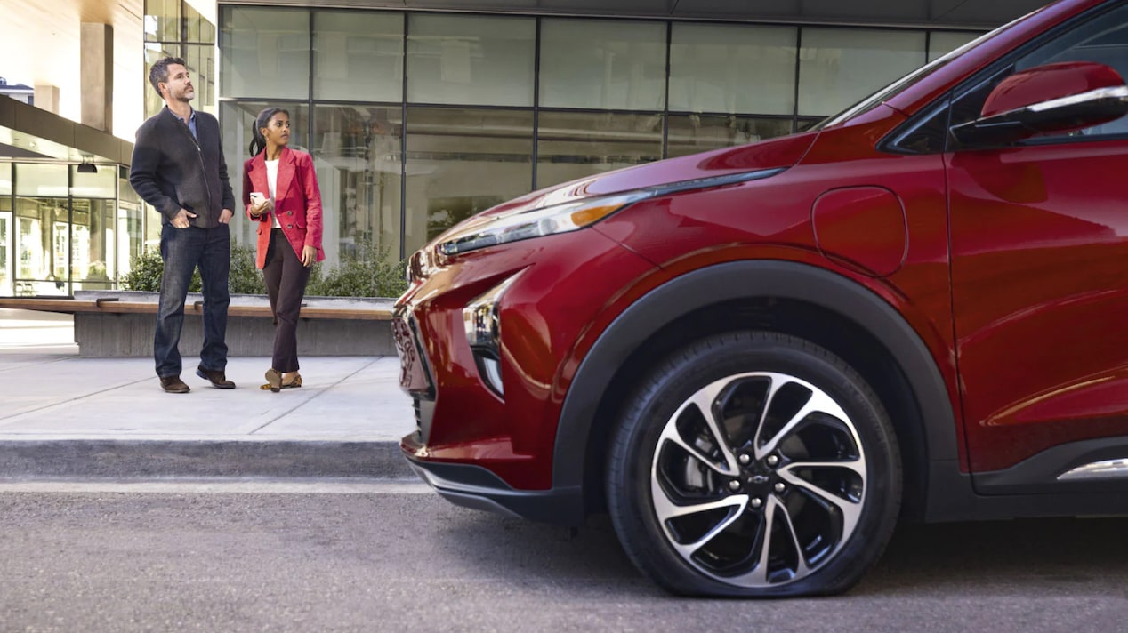 A Couple Standing on the Sidewalk Next to Their Chevrolet EV with a Flat Tire