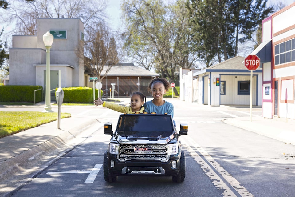 Two Kids in a Mini Play Car Driving Down the Road