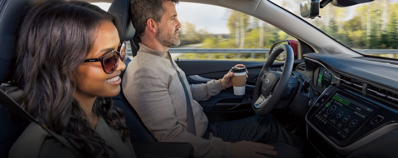 A couple driving down the road using Super Cruise hands-free driving assistance technology