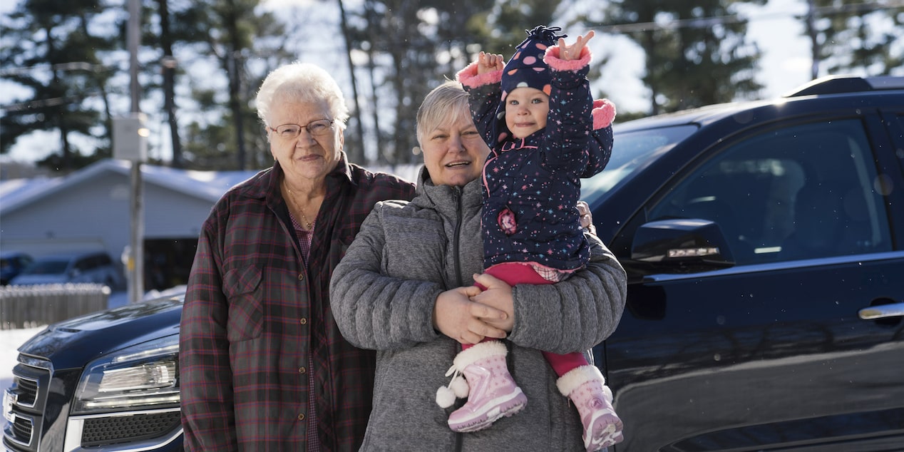 Grandparents and Granddaughter Standing in Front of Vehicle